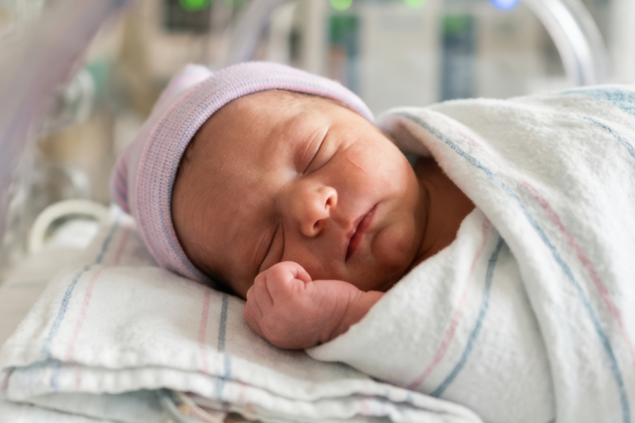 Newborn baby sleeping peacefully while wrapped in a hospital blanket and wearing a knit cap, symbolizing newborn care, maternity, or infant health.
