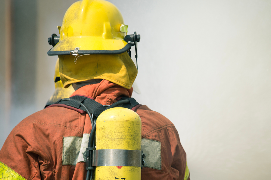 Firefighter wearing protective gear and an air tank, viewed from behind.