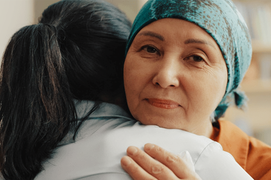 Person wearing a headscarf embraces a loved one during cancer treatment.